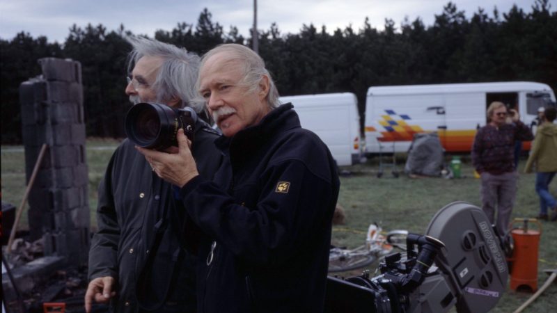 Michael Haneke hält ein Kameraobjekt auf höhe seines Köpfes. Hinter ihm steht Michael Haneke.