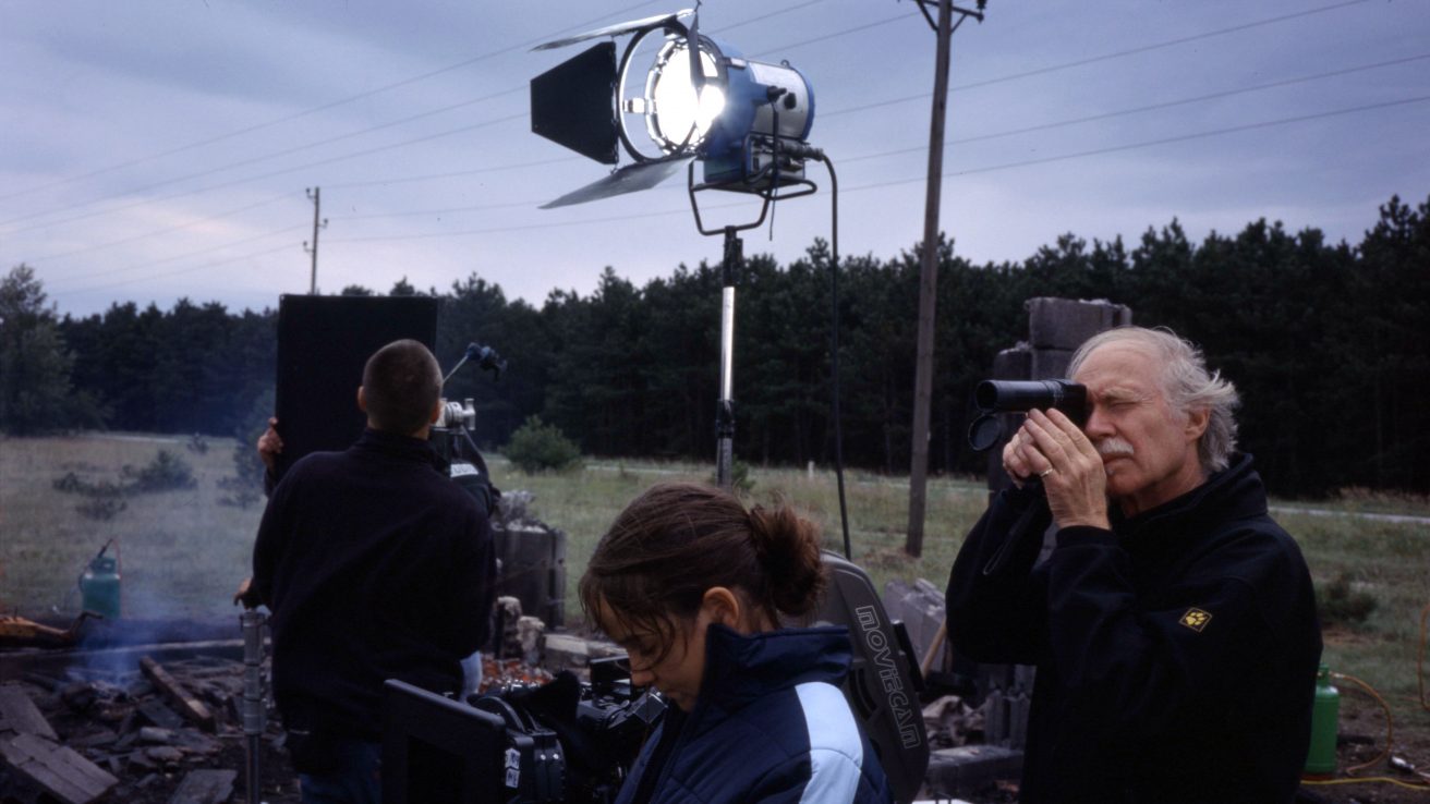 Jürgen Jürges schaut durch ein Kameraobjektiv. Die Crew baut neben ihm das Set auf.