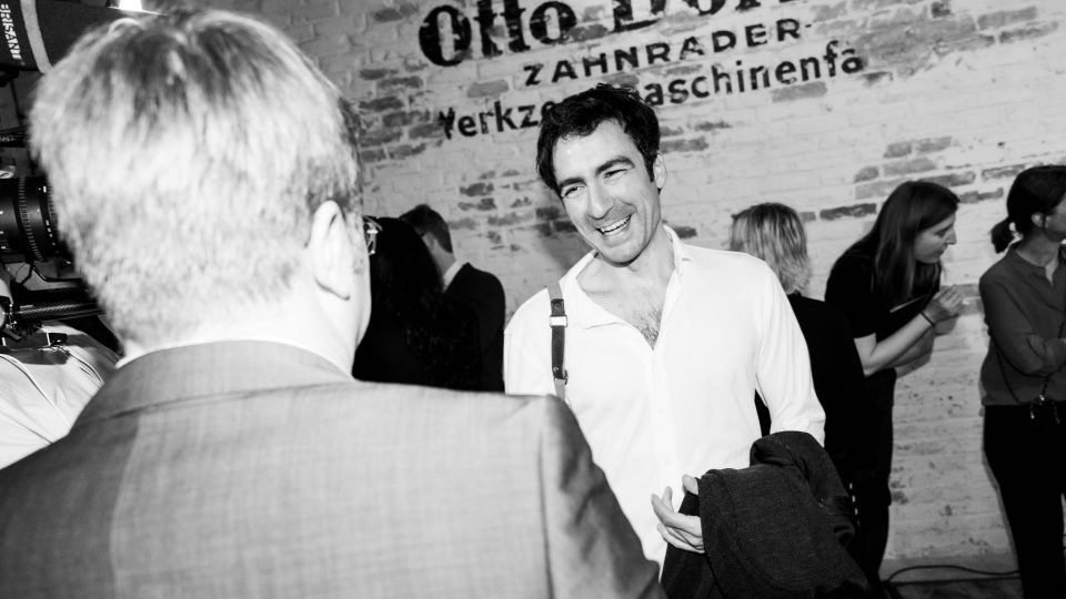 schwarz-weiß Bild: Ilker Çatak lächelt einen Mann an.