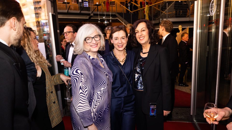 Zu sehen sind drei lächelnde Frauen namens Claudia Loewe, Anne Leppin, Maria Köpf. Sie tragen blaue Kleidung in verschieden Optiken.