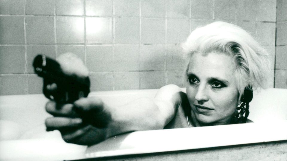 Hannah Schygulla sitz in einer Badewanne mit einer Pistole in der Hand, welche sie in die Ferne richtet.